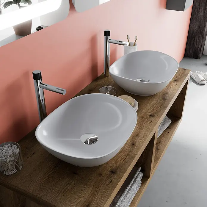 Kiamami Valentina Badmöbel-Set - Holz mittel - Zwei weiße ovale Aufsatzwaschbecken und Chromarmaturen auf einem hölzernen Doppelwaschtisch im modernen Bad mit rosa Wand.