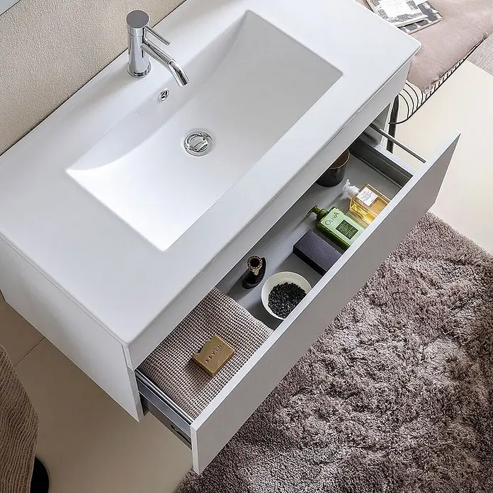 Kiamami Valentina Badmöbel-Set - Weiß - Modernes weißes Badezimmerwaschtisch mit integriertem Waschbecken und offener Schublade, die Badartikel zeigt.