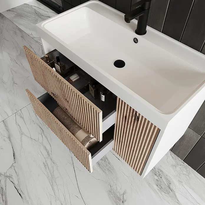 Kiamami Valentina Badmöbel-Set - Braun - Weißer Badunterschrank mit integriertem Waschbecken und zwei offenen Schubladen mit Holzlamellenfronten, die Toilettenartikel und ein Handtuch zeigen.