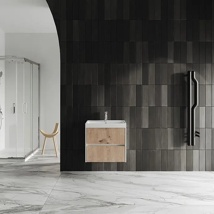 Kiamami Valentina Badmöbel-Set - Braun - Weißer Badezimmerschrank mit Waschbecken und hellen Holzlamellenfronten, in einem modernen Bad mit dunklen Fliesenwänden.