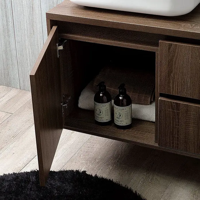 Kiamami Valentina Badmöbel-Set - Holz dunkel - Dunkelbrauner Badezimmerschrank aus Holz mit offener Tür, der Stauraum und Handtücher unter einem weißen Waschbecken zeigt.