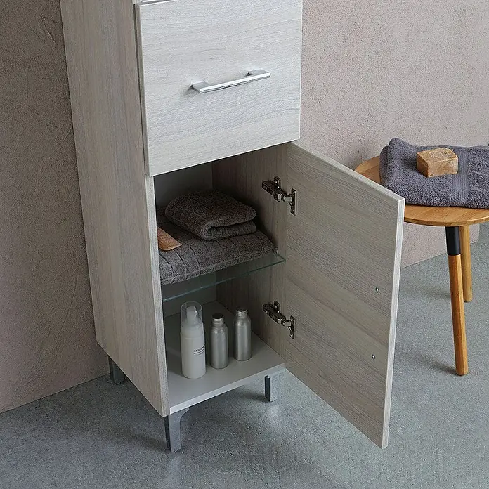 Kiamami Valentina Badmöbel-Set - Grau - Heller Badezimmerschrank in Holzoptik mit offener Tür, die Handtücher und Flaschen auf Ablagen zeigt, und einer oberen Schublade.