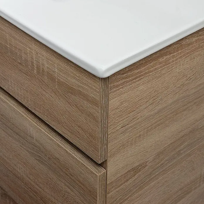 Kiamami Valentina Badmöbel-Set - Helles Holz - Nahaufnahme eines hellbraunen Waschtischunterschranks in Holzoptik mit weißer Keramikplatte.