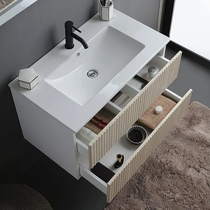 Kiamami Valentina Badmöbel-Set - Braun - Weißer Waschtischunterschrank mit integriertem Waschbecken und schwarzem Wasserhahn. Zwei offene helle Holzlamellen-Schubladen zeigen Badezimmerutensilien.