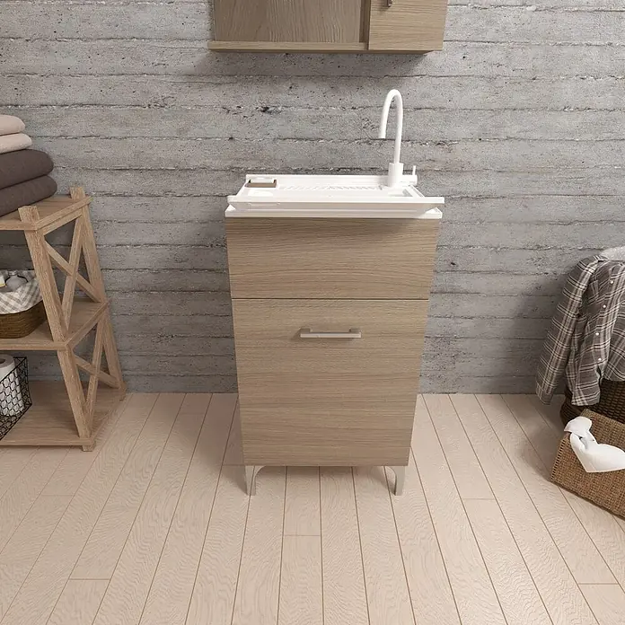 Kiamami Valentina Badmöbel-Set - Holz mittel - Heller Holz-Waschschrank mit integriertem weißem Waschbecken und Wasserhahn, zwei Schubladen mit silbernen Griffen, in einem modernen Hauswirtschaftsraum.