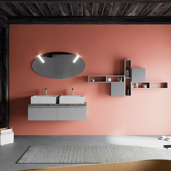 Kiamami Valentina Badmöbel-Set - Grau - Modernes Badezimmer mit Doppelwaschtisch, weißen Waschbecken, grauen Schränken, modularen Wandregalen und beleuchtetem Ovalspiegel.