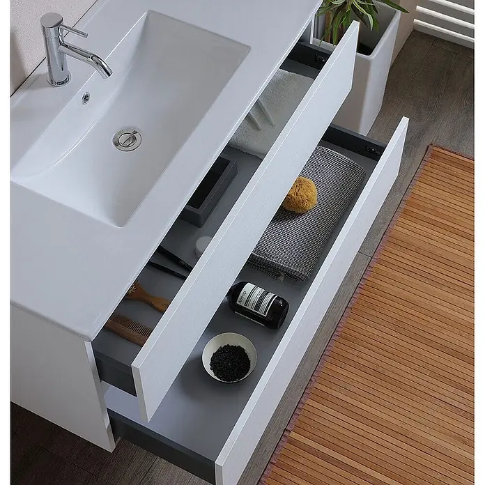 Kiamami Valentina Badmöbel-Set - Weiß - Weißer Badezimmerschrank mit integriertem Waschbecken und offenen grauen Schubladen.
