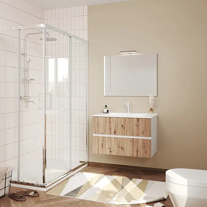 Kiamami Valentina Badmöbel-Set - Helles Holz - Moderne Badezimmer mit Glasduschkabine und wandmontiertem Waschtisch mit weißem Becken und zwei Holzschubladen, darüber ein Spiegel.