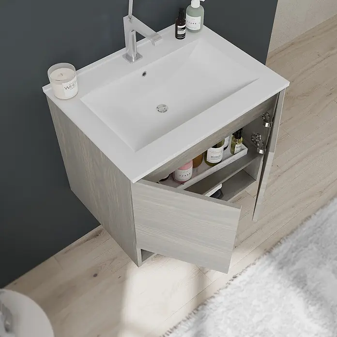 Kiamami Valentina Badmöbel-Set - Helles Holz - Hellgrauer Holzwaschtisch mit weißem integriertem Waschbecken und silbernem Wasserhahn. Tür offen, zeigt Toilettenartikel.