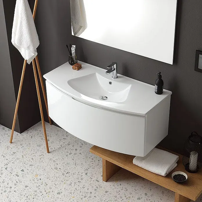 Kiamami Valentina Badmöbel-Set - Weiß - Weißer Badunterschrank mit integriertem Waschbecken an dunkler Wand, in modernem Badambiente mit Holzbank darunter.
