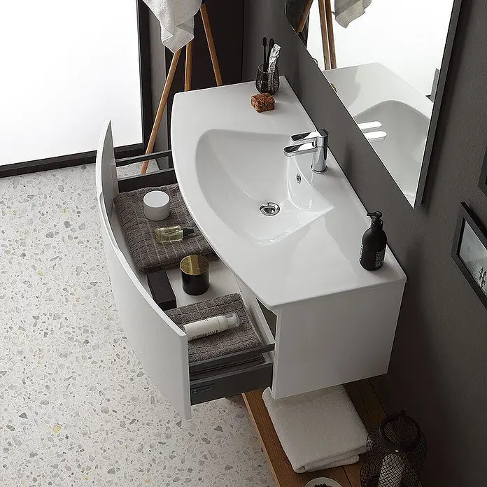 Kiamami Valentina Badmöbel-Set - Weiß - Weißer wandmontierter Badunterschrank mit integriertem Waschbecken und offener gebogener Schublade mit Toilettenartikeln.