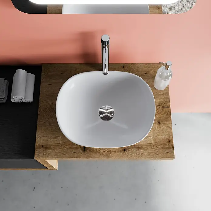 Kiamami Valentina Badmöbel-Set - Grau - Blick von oben auf einen modernen Badezimmerwaschtisch mit weißem ovalem Waschbecken, Chromarmatur und Holzarbeitsplatte vor einer rosa Wand.