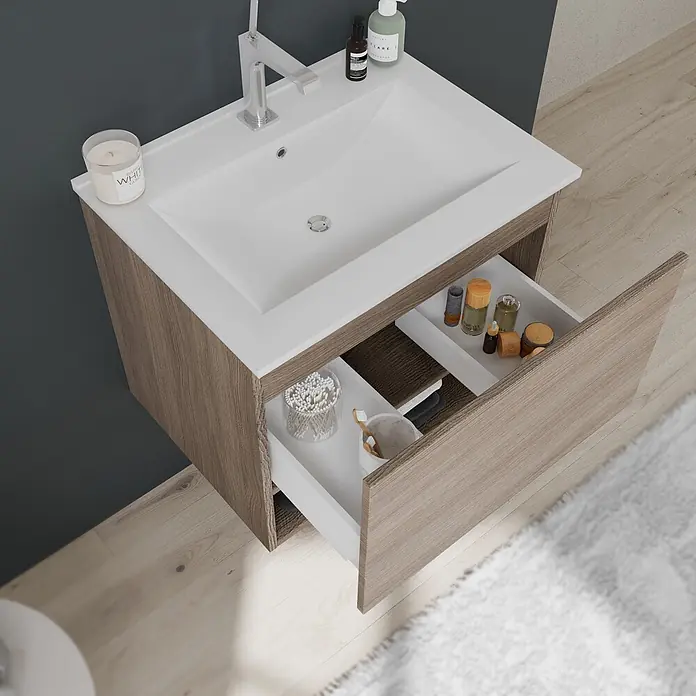 Kiamami Valentina Badmöbel-Set - Holz mittel - Waschtischunterschrank aus heller Holzmaserung mit weißem integriertem Waschbecken, Chromarmatur und geöffneten Schubladen mit Pflegeprodukten.