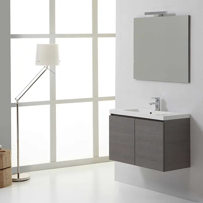 Kiamami Valentina Badmöbel-Set - Grau - Wandmontierter Badunterschrank mit dunkler Holzoptik, weißem integrierten Waschbecken und rechteckigem Spiegel mit Chromleuchte.