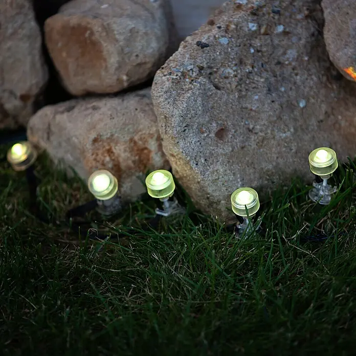 Ledvance Smart+ LED-Panel Gardenspot Mini RGBW 3ST - Dimmbarkeit: Dimmbar, Durchmesser: 23 mm, Leuchtmittel: LED, IP65, II - Kleine, beleuchtete Gartenleuchten mit klaren Gehäusen leuchten im grünen Gras neben großen Steinen als Akzentbeleuchtung.