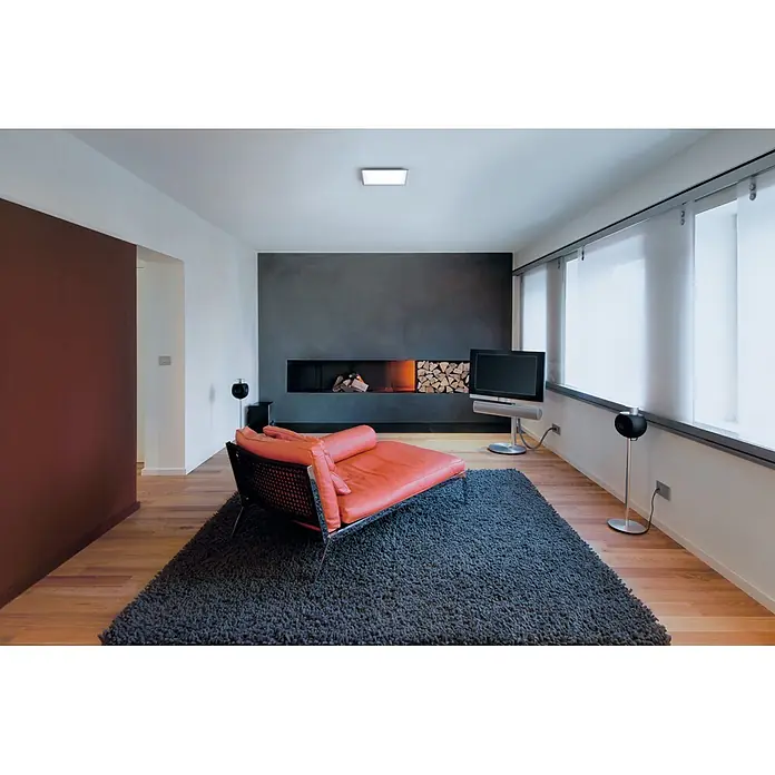 Ledvance Smart+ WiFi LED-Panel Planon Plus - L x B x H: 300 x 300 x 56 mm, Weiß, Warmweiß - Ein orangefarbenes Ledersofa mit schwarzem Metallgestell auf einem zotteligen grauen Teppich in einem modernen Wohnzimmer.
