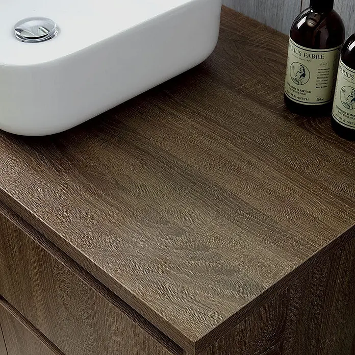 Kiamami Valentina Badmöbel-Set - Holz dunkel - Dunkelbrauner Waschtischunterschrank in Holzmaserung mit weißem Waschbecken und zwei Flaschen.