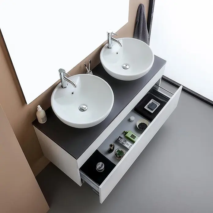Kiamami Valentina Badmöbel-Set - Weiß - Modernes Doppelwaschtisch mit weißen Aufsatzwaschbecken, Chromarmaturen, dunkler Arbeitsplatte und offener Schublade.