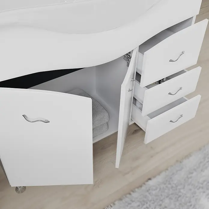 Kiamami Valentina Badmöbel-Set - Weiß - Weißer Badezimmerschrank mit offener Tür, grauen Handtüchern und offenen Schubladen mit silbernen Griffen.