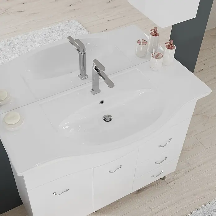 Kiamami Valentina Badmöbel-Set - Weiß - Weißer Badezimmerschrank mit integriertem Waschbecken und Chromarmaturen, ergänzt durch ein roségoldenes Accessoire-Set. Auf hellem Holzboden neben einem weißen Teppich.