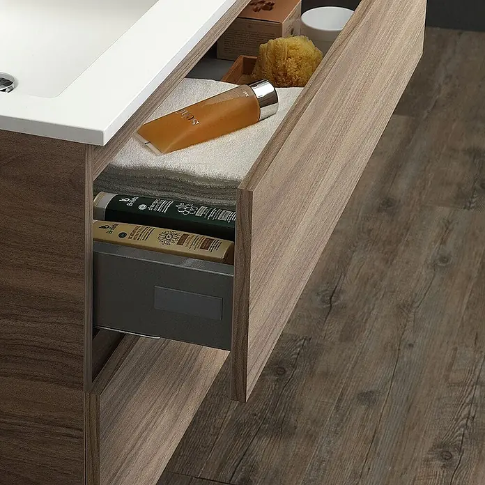 Kiamami Valentina Badmöbel-Set - Helles Holz - Waschtisch mit Holzmaserung und weißem Waschbecken, offene Schubladen zeigen Handtücher und Toilettenartikel.