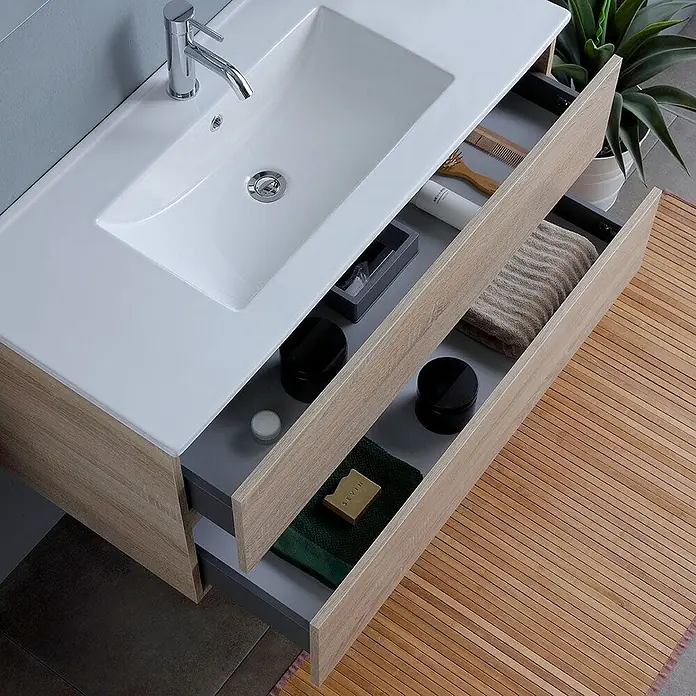 Kiamami Valentina Badmöbel-Set - Braun - Helles Badezimmer-Waschtisch mit weißem Keramikbecken und zwei offenen Schubladen mit Pflegeprodukten.