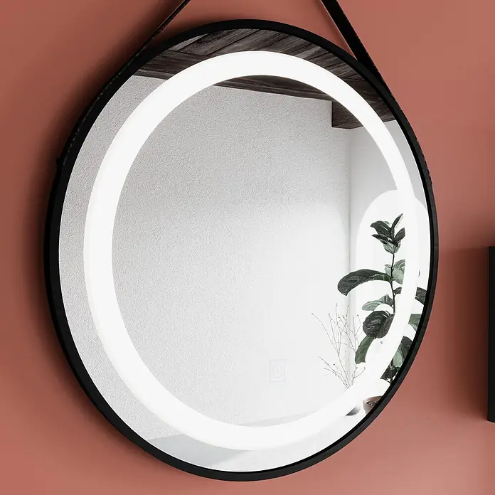 Kiamami Valentina Badmöbel-Set - Grau - Runder LED-Spiegel mit schwarzem Rahmen, beleuchtet und einen Raum mit Pflanze reflektierend.