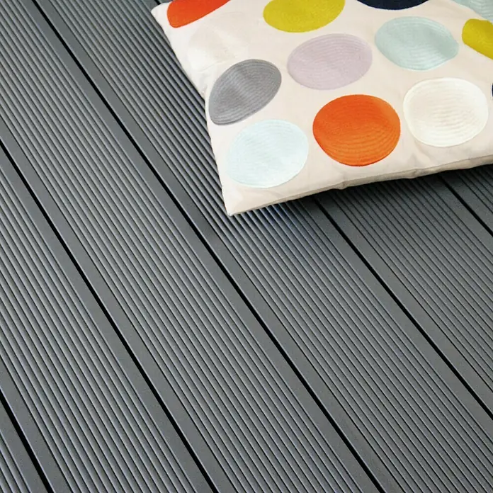 Kovalex WPC-Terrassendiele Exklusiv nach Maß - 440 x 14,5 x 2,6 cm, Steingrau - Terrassendielen aus Verbundmaterial mit einem Kissen mit bunten Punkten. Die Dielen sind grau und haben eine geriffelte Oberfläche.