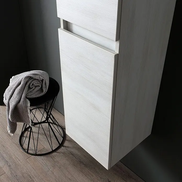 Kiamami Valentina Badmöbel-Set - Grau - Heller Holzschrank mit teilweise geöffneter Schublade, auf Holzboden neben schwarzem Hocker mit grauer Decke.