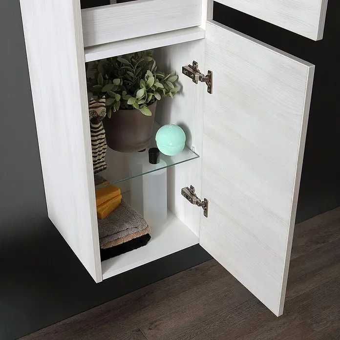 Kiamami Valentina Badmöbel-Set - Grau - Weißer Wandschrank aus Holz, offen, mit Glasregal, das eine Pflanze, Badebombe und Pflegeprodukte zeigt.