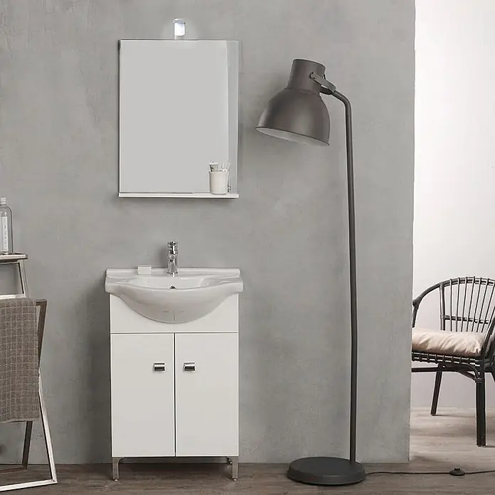 Kiamami Valentina Badmöbel-Set - Weiß - Weißer Badezimmer-Waschtischunterschrank mit integriertem Waschbecken und Stauraum, daneben eine hohe, dunkle Stehleuchte.
