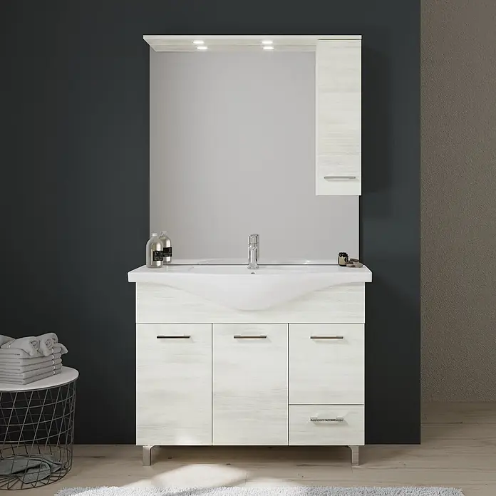 Kiamami Valentina Badmöbel-Set - Helles Holz - Weißer Badunterschrank mit Holzoptik, integriertem Waschbecken, Spiegel und Wandschrank vor dunkler Wand.