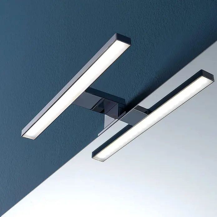 Kiamami Valentina Badmöbel-Set - Grau - Moderne LED-Spiegelleuchte mit zwei linearen Chrom-Lichtbalken, an blauer Wand über einem Spiegel montiert.