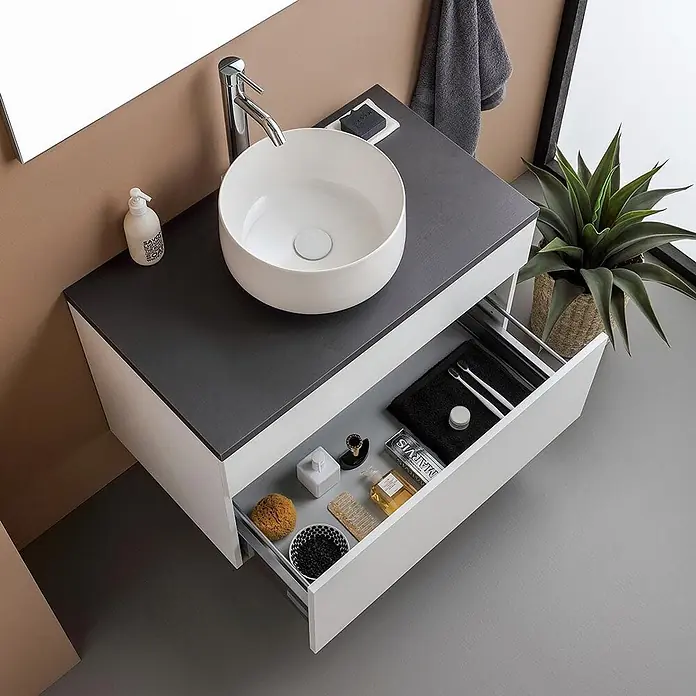 Kiamami Valentina Badmöbel-Set - Weiß - Moderner weiß-dunkelgrauer Badunterschrank mit Aufsatzwaschbecken und geöffneter Schublade mit Toilettenartikeln.
