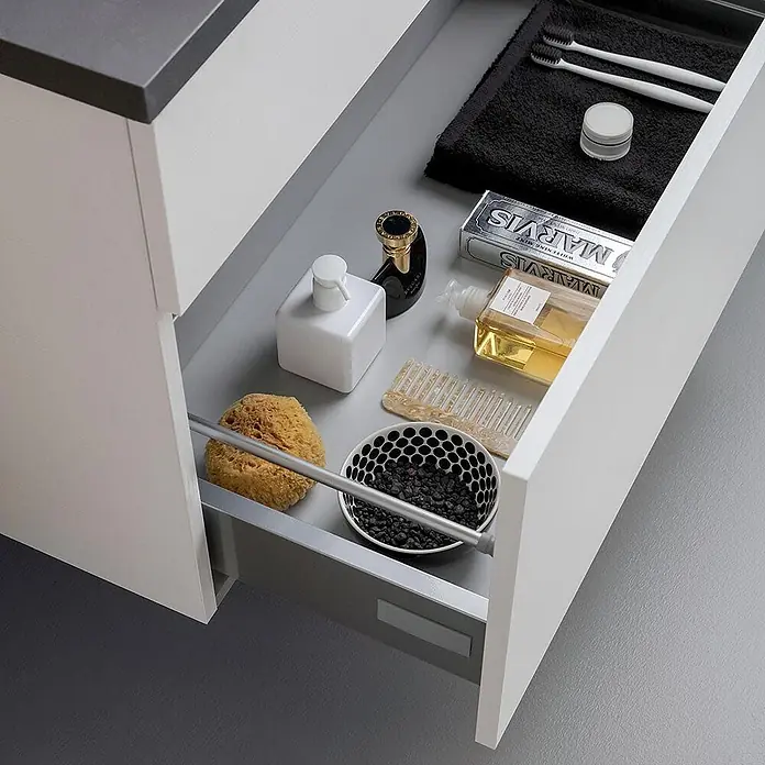 Kiamami Valentina Badmöbel-Set - Weiß - Offene weiße Badezimmerschublade mit grauem Innenraum, ordentlich organisiert mit Toilettenartikeln wie Zahnbürsten, Zahnpasta, Lotion und Schwämmen.
