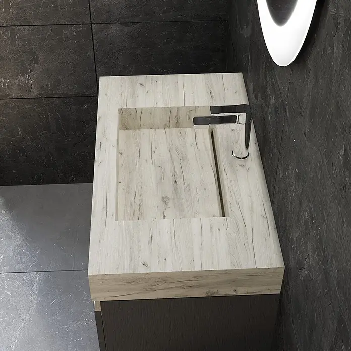 Kiamami Valentina Badmöbel-Set - Grau - Badezimmermöbel mit integriertem hellen Holzoptik-Waschbecken und Chromarmatur, vor dunklen Fliesenwänden und Boden.