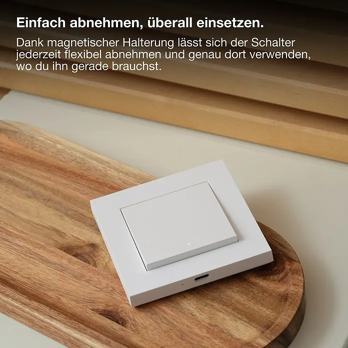 Osram Smart+ Schalter magnetischer Wandschalter 1G matter - Weiß, Innen - Ein weißer, magnetischer Smart-Schalter im minimalistischen Design liegt auf einem Holzteller. Er ist flexibel positionierbar.