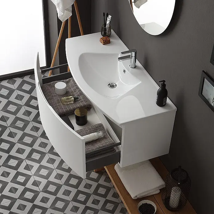 Kiamami Valentina Badmöbel-Set - Weiß - Weiße wandmontierte Badezimmervanitee mit integriertem Waschbecken und offener, gebogener Schublade mit Toilettenartikeln und Handtüchern.