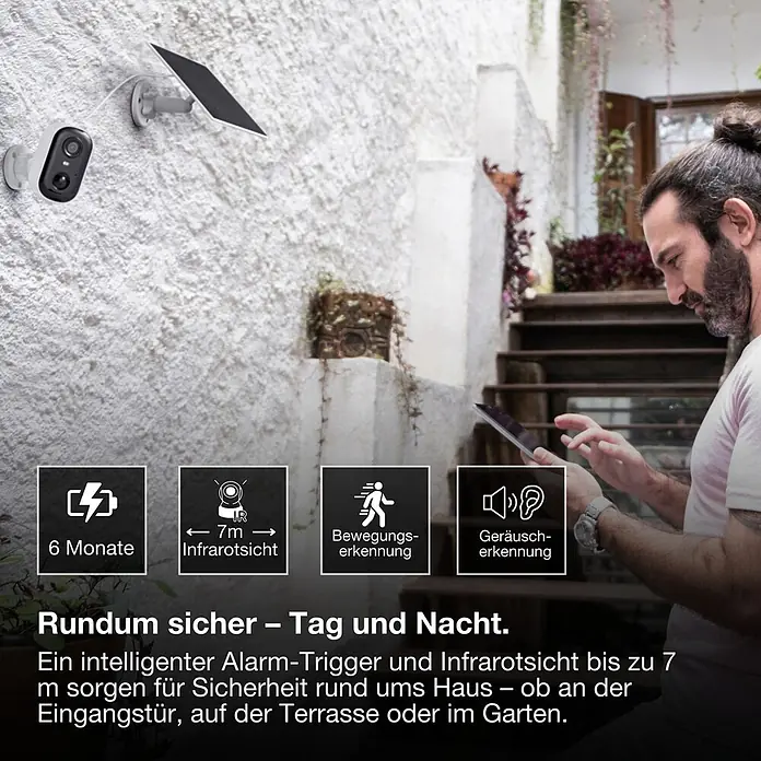Osram Smart+ Überwachungskamera Battery Solar - Weiß - Weiß-schwarze Überwachungskamera mit Solarpanel an Hauswand. Mann nutzt Tablet, zeigt Smart-Home-Monitoring.