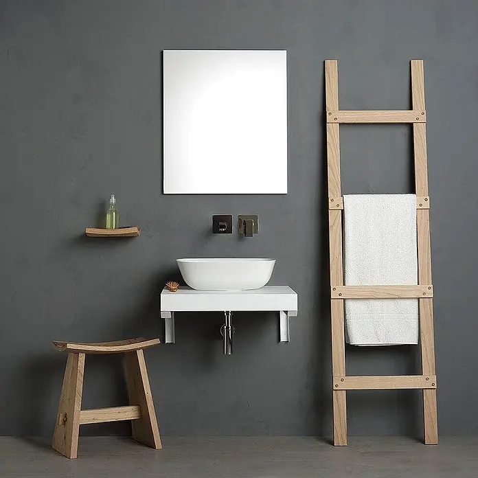 Kiamami Valentina Badmöbel-Set - Weiß - Modernes Badezimmer mit weißem Waschtisch, rechteckigem Spiegel, hellem Holzhocker und Handtuchleiter mit weißen Handtüchern.