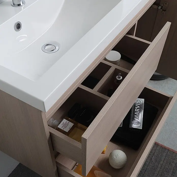 Kiamami Valentina Badmöbel-Set - Beige - Badezimmermöbel aus hellem Holz mit weißem Waschbecken und offenen Schubladen mit Toilettenartikeln.