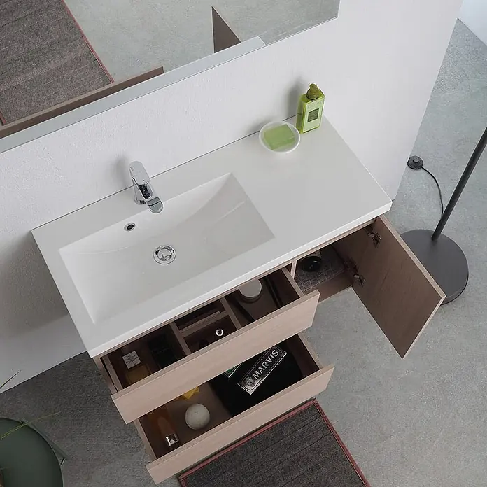 Kiamami Valentina Badmöbel-Set - Beige - Heller Holzbadschrank mit weißem Waschbecken, Chromarmatur, offener Tür und zwei offenen Schubladen mit Toilettenartikeln.