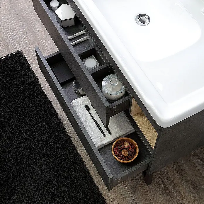 Kiamami Valentina Badmöbel-Set - Grau - Dunkelgrauer Badschrank mit weißem Waschbecken und offenen Schubladen, die Toilettenartikel zeigen.