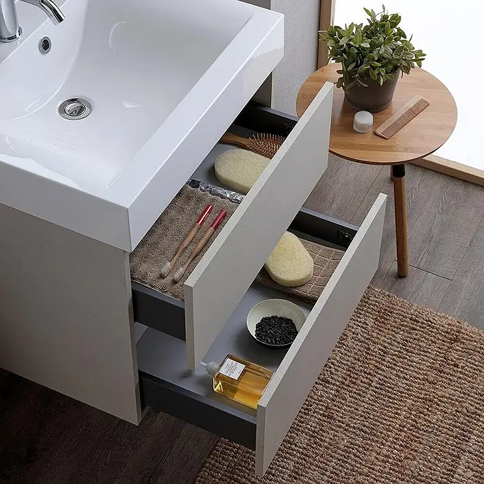 Kiamami Valentina Badmöbel-Set - Grau - Hellergrauer Badschrank mit weißem Waschbecken und zwei geöffneten Schubladen für Toilettenartikel.