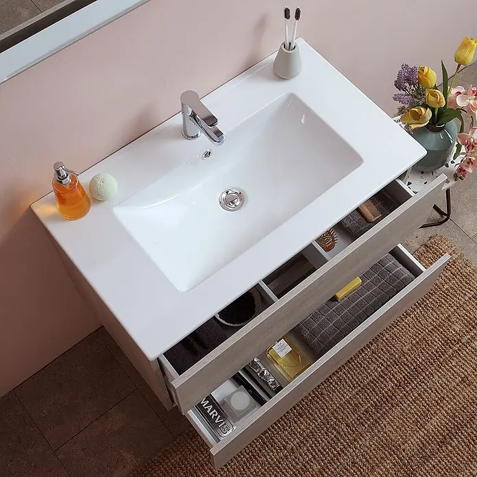 Kiamami Valentina Badmöbel-Set - Helles Holz - Ein Badezimmerschrank in heller Holzoptik mit weißem Einbauwaschbecken und zwei geöffneten Schubladen mit Stauraum für Toilettenartikel.