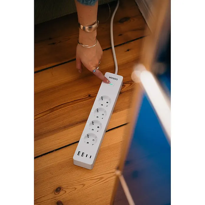Osram Smart+ Smart-Steckdosenleiste 2. Gen. 2 USB-A, 2 USB-C - Weiß - Weiße Steckdosenleiste mit mehreren Steckdosen und USB-Anschlüssen wird auf Holzboden eingeschaltet.