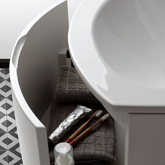 Kiamami Valentina Badmöbel-Set - Weiß - Weißer, gebogener Badunterschrank mit Waschbecken, darin Handtücher und Toilettenartikel.