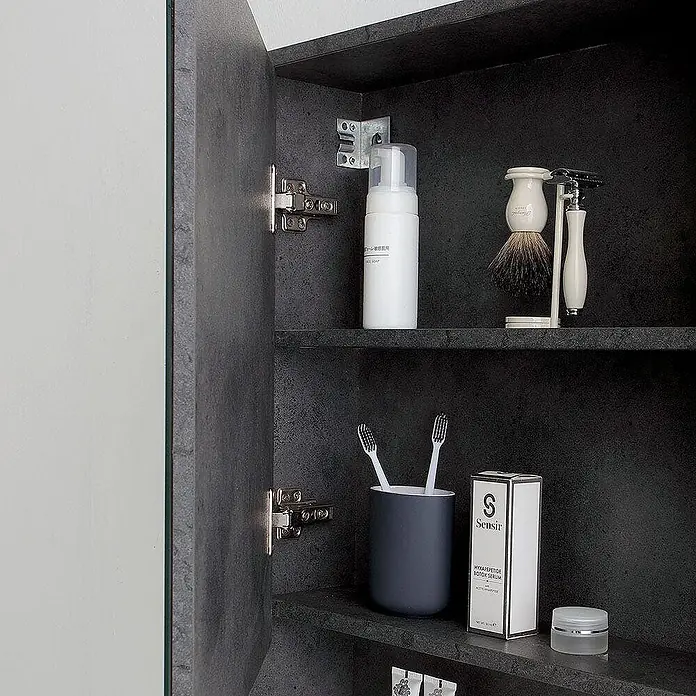 Kiamami Valentina Badmöbel-Set - Grau - Verschiedene Toilettenartikel wie Reinigungsschaum, Rasierset und Zahnbürsten ordentlich in einem dunkelgrauen Badezimmerschrank aufbewahrt.