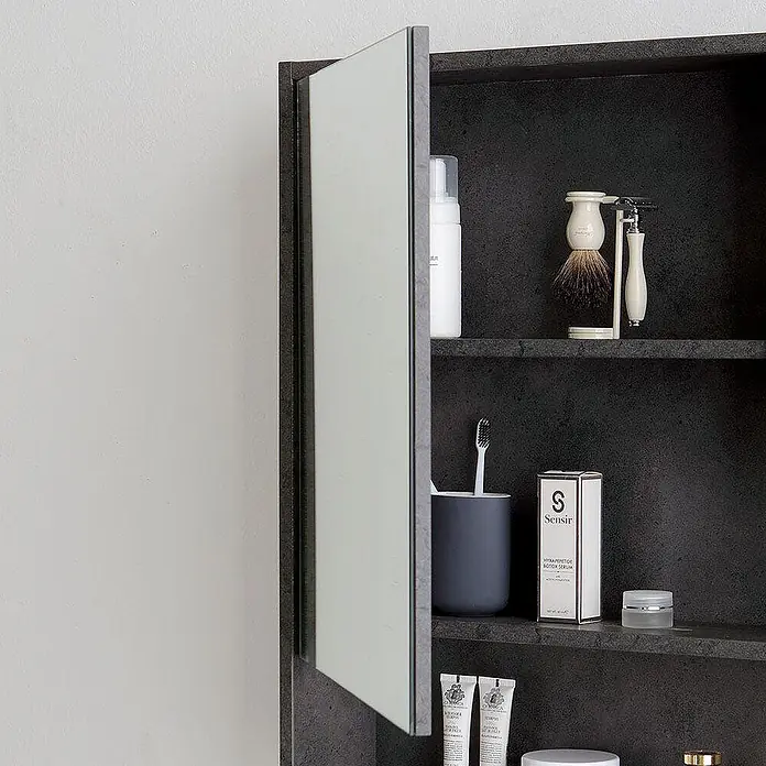 Kiamami Valentina Badmöbel-Set - Grau - Offener dunkelgrauer Badezimmerschrank mit Spiegeltür, gefüllt mit Toilettenartikeln: Rasierset, Zahnbürste, Hautpflegeprodukte.