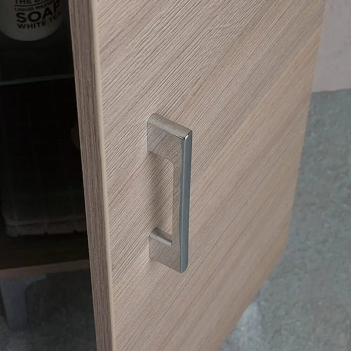 Kiamami Valentina Badmöbel-Set - Holz mittel - Helle Holzmaserung-Schranktür mit Chromgriff, dahinter gelagerte Gegenstände.